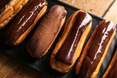 Plate with sweet chocolate eclairs on wooden table, closeup