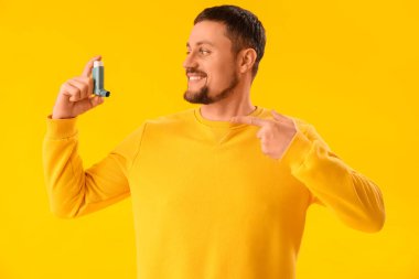 Sarı arka planda astım spreyi olan adam.