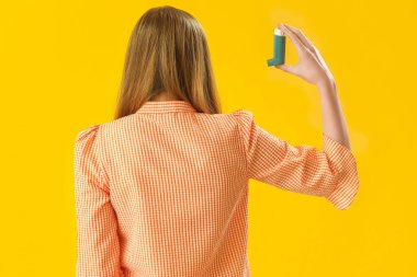 Young woman with inhaler on yellow background, back view