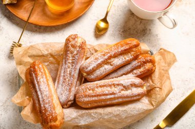 Bowl of delicious eclairs with sugar powder on light background, closeup