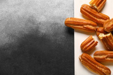 Board with sweet eclairs on black and white background