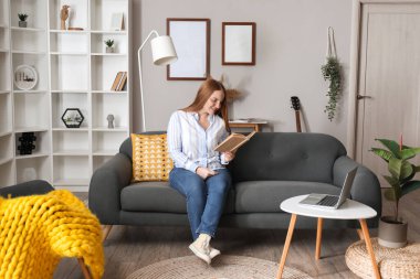 Evdeki siyah koltukta kitap okuyan güzel bir kadın.