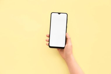 Female hand with mobile phone on yellow background
