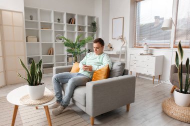 Young man using mobile phone on grey couch in living room