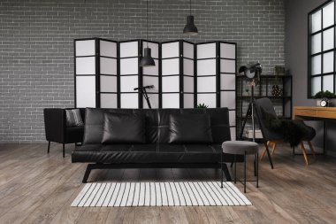 Interior of stylish office with black couch, workplace and folding screen