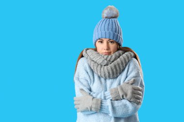 Frozen young woman in winter clothes on blue background