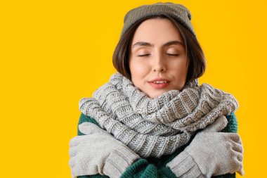Frozen young woman in winter clothes on yellow background, closeup