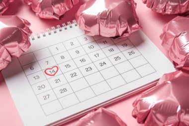 Calendar with marked date of Valentine's Day and balloons on pink background, closeup
