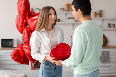 Young man greeting his girlfriend with gift in kitchen on Valentine's Day