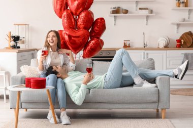 Young couple with glasses of wine celebrating Valentine's Day in kitchen