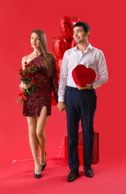 Güllere aşık genç bir çift ve kırmızı arka planda hediye. Sevgililer Günü kutlaması