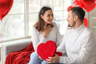 Young man greeting his wife with gift at home on Valentine's Day