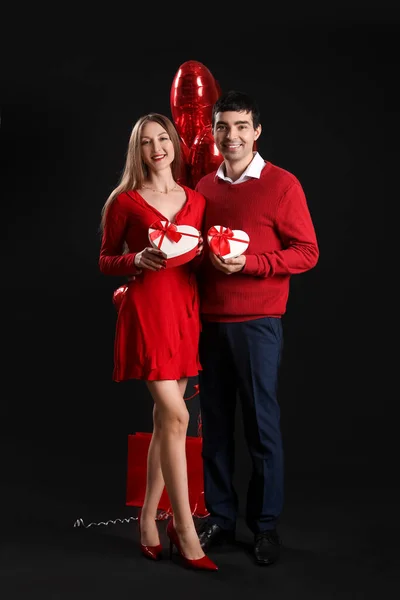 Young couple in love with gifts on black background. Valentine\'s Day celebration