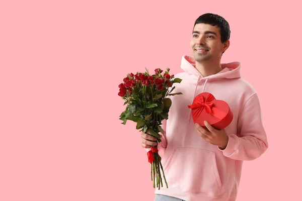 Young man with roses and gift on pink background. Valentine\'s Day celebration