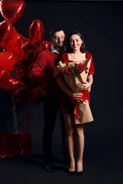 Happy couple in love with roses and balloons on black background. Valentine\'s Day celebration