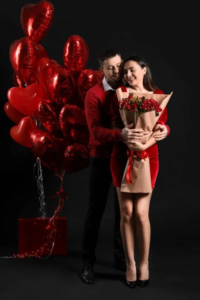 Happy couple in love with roses and balloons on black background. Valentine's Day celebration