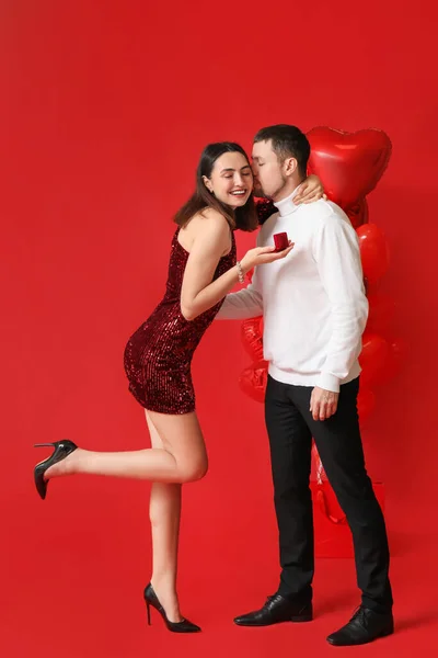 Engaged couple in love with ring on red background. Valentine\'s Day celebration