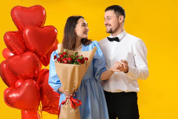 Happy couple in love with roses and balloons on yellow background. Valentine\'s Day celebration