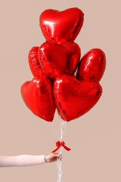 Woman with heart-shaped balloons for Valentine\'s Day near beige wall