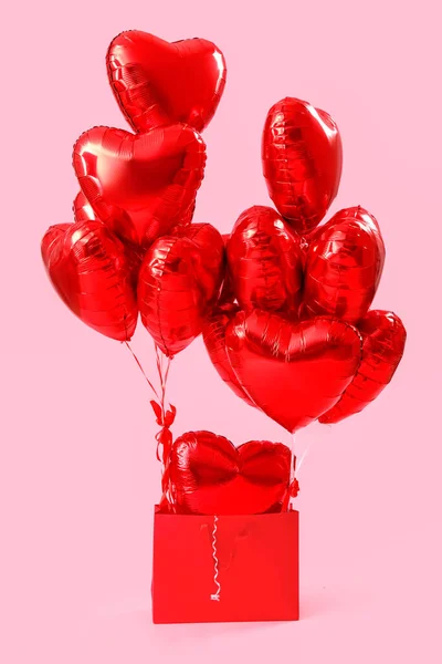 Shopping bag with heart-shaped balloons for Valentine\'s Day on pink background