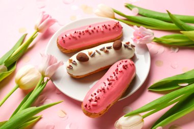 Plate with delicious glazed eclairs and tulips on pink background