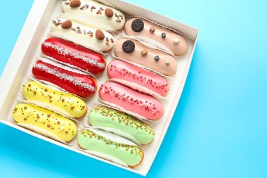 Box with various glazed eclairs on blue background