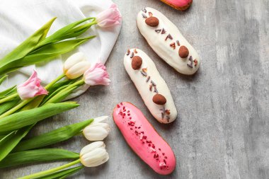 Delicious glazed eclairs and tulips on grey table