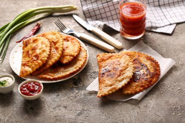 Cheburek soslu tabak, acı biber, soğan, domates suyu ve arkaplanda çatal bıçak.