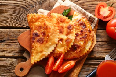 Tahta kesme tahtası lezzetli chebureks ve ahşap arka planda domates dilimleri