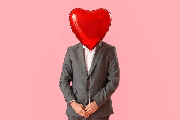 Man hiding face behind heart-shaped balloon on pink background. Valentine\'s Day celebration
