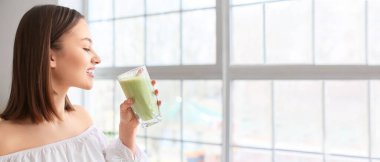 Pretty young woman drinking healthy green smoothie at home