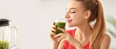Pretty young woman drinking green smoothie at home