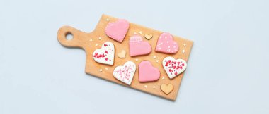 Wooden board with tasty heart shaped cookies on light background. Valentine's Day celebration