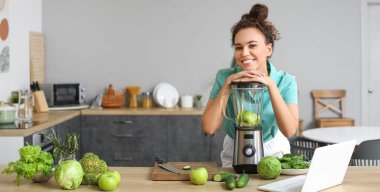 Young African-American woman making fresh smoothie in kitchen