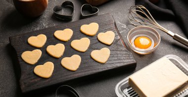 Board with raw heart shaped cookies and ingredients on dark background. Valentines Day celebration