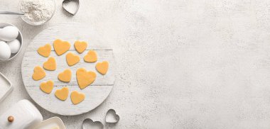 Board with raw heart shaped cookies and ingredients on light background with space for text. Valentines Day celebration