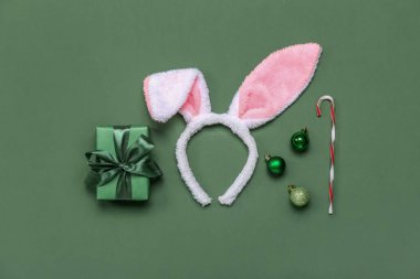 Bunny ears with Christmas balls, gift and candy cane on green background