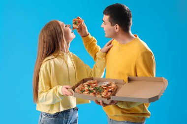 Young man feeding his girlfriend with tasty pizza on blue background