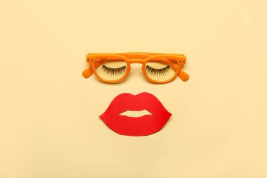 Face made of fake eyelashes, eyeglasses and paper lips on color background
