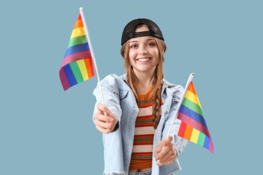 Beautiful young woman with LGBT flags on blue background