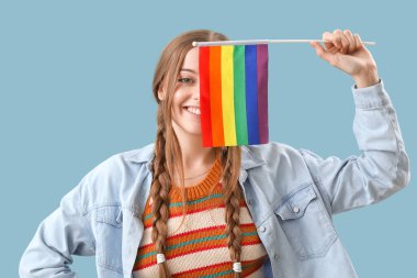 Beautiful young woman with LGBT flag on blue background