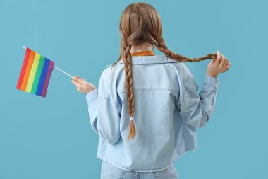 Beautiful young woman with LGBT flag on blue background, back view