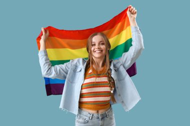 Beautiful young woman with LGBT flag on blue background