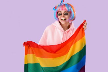 Beautiful young woman with candy and LGBT flag on lilac background