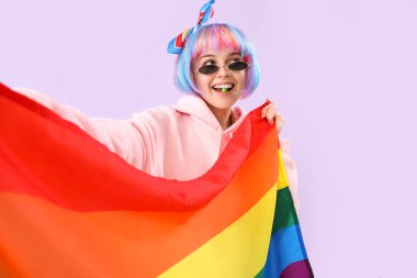 Beautiful young woman with candy and LGBT flag on lilac background