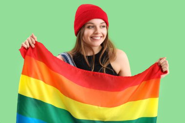 Beautiful young woman with LGBT flag on green background
