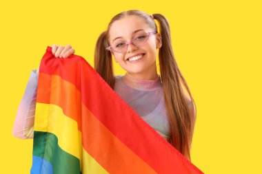 Beautiful young woman in sunglasses with LGBT flag on yellow background