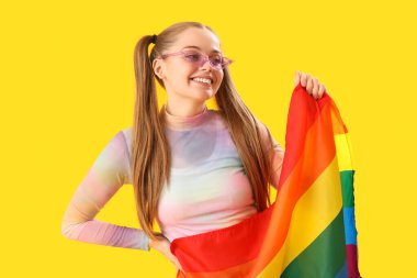 Beautiful young woman in sunglasses with LGBT flag on yellow background