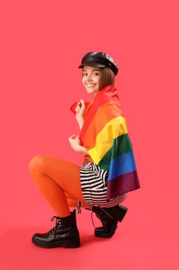 Beautiful young woman in hat with LGBT flag sitting on red background