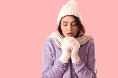 Frozen young woman in winter clothes on pink background